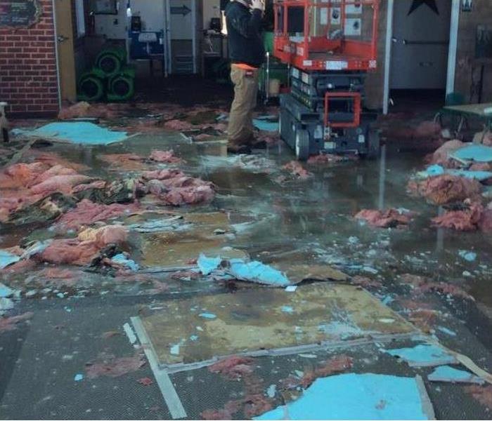 A person standing on wet floor, insulation all over the floor. Concept of storm damage in a Daycare